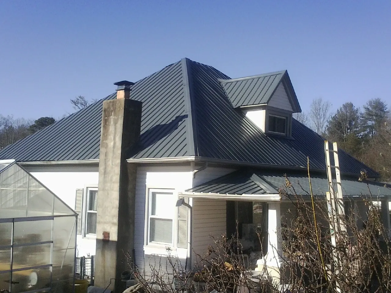 Dark blue standing seam metal roof on a white farmhouse with dormer — Slate & Tile Roof Repair by Roofing Brothers in Corapeake