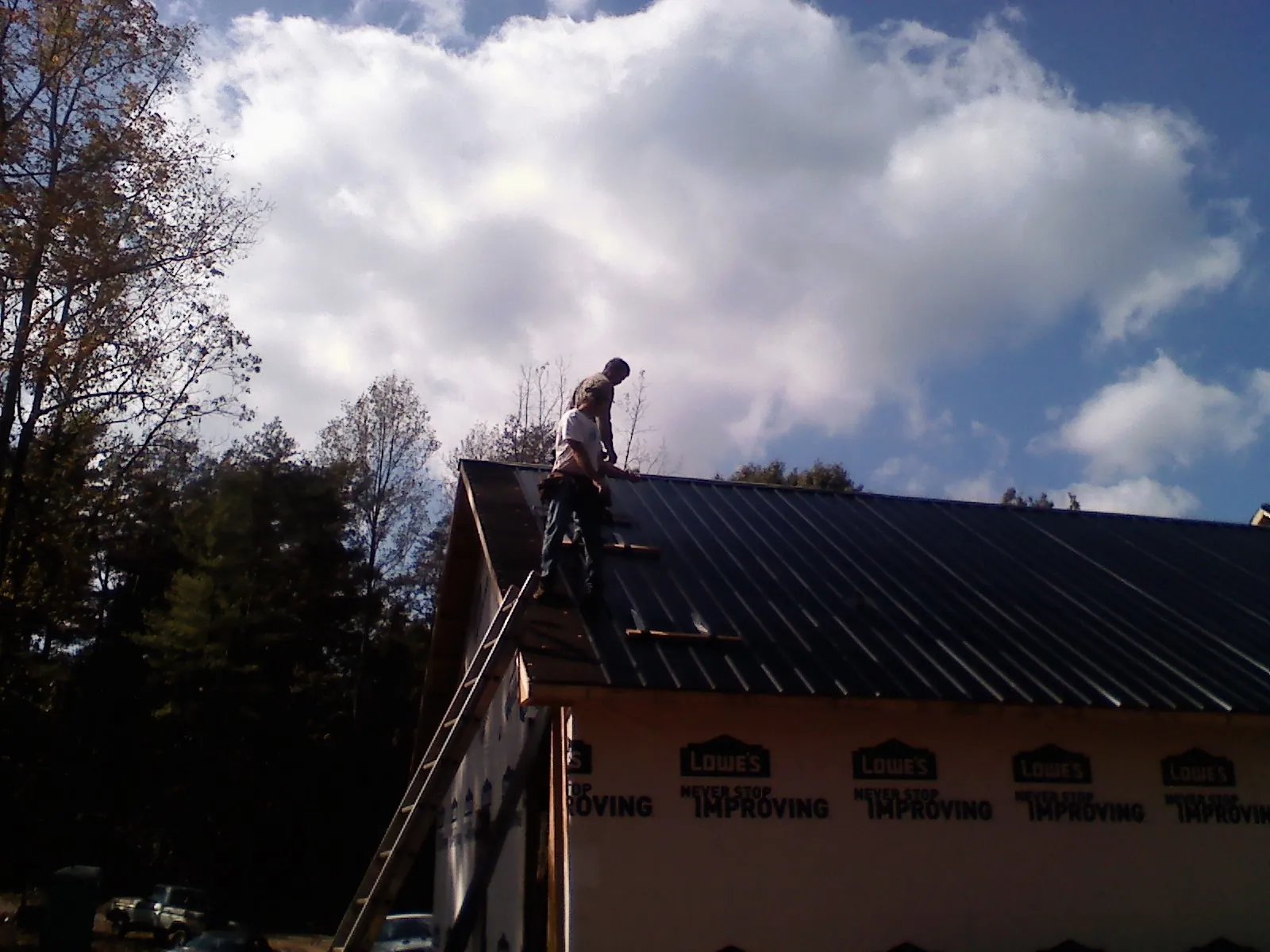 Roofer fastening dark metal panels high against a cloudy sky, from a Roof Inspection job in Corapeake